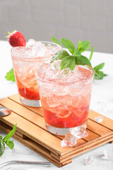 Cold summer strawberry cocktail mojito, margarita, daiquiri. Two glasses with fresh strawberry soda drink with ice cubes and mint leaves on light grey background. Iced strawberry lemonade, close up