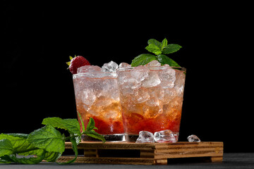Cold summer strawberry cocktail mojito, margarita, daiquiri. Two glasses with fresh strawberry soda drink with ice cubes and mint leaves on dark background. Iced strawberry lemonade, close up