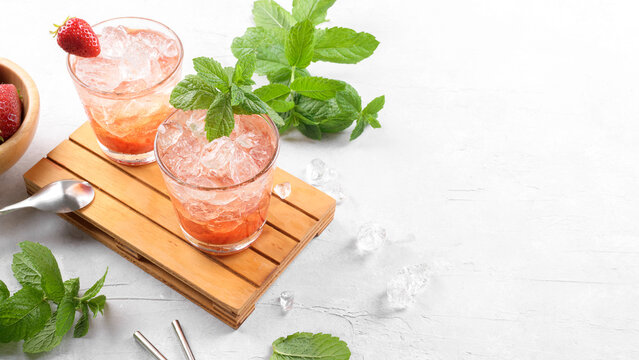 Cold summer strawberry cocktail mojito, margarita, daiquiri. Two glasses with fresh strawberry soda drink with ice cubes and mint leaves on light grey background. Iced strawberry lemonade, copy space