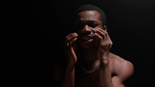 Portrait black African American man with pumped naked torso sings song emotionally waving his arms on black background. Shooting clip of rap artist. Man sings rapping song.