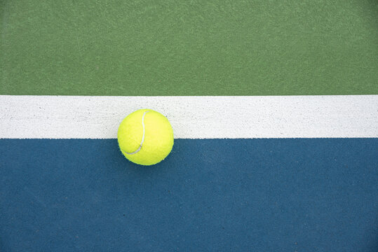 Top view of a tennis ball hitting inside the line of the doubles sideline on a court.