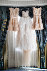 Wedding and bridesmaids dresses hanging by the window