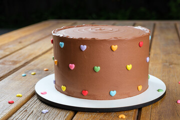 Closeup of chocolate cake topped with semisweet chocolate ganache. Decorated with mini colored...