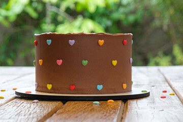 Closeup of chocolate cake topped with semisweet chocolate ganache. Garden in the background_side...
