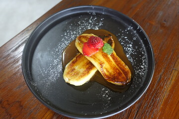 Fried banana food served on a black plate, on a wooden table.
