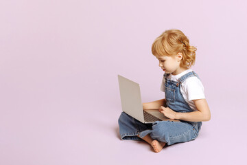 The girl on a light pink background sits with a laptop.