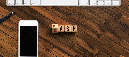 cubes with message CRASH and CASH surrounded by smartphone and keyboard on wooden surface