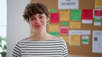 Happy young woman student standing in front of employment noticeboard, looking at camera.