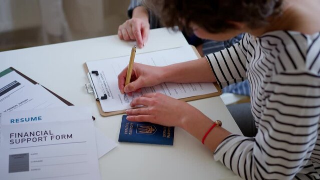 Senior woman volunteer helping Ukrainian woman to fill in forms at asylum centre.