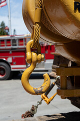 Yellow winch hook hanging from its cable reel. In the background is a fire engine and a flag