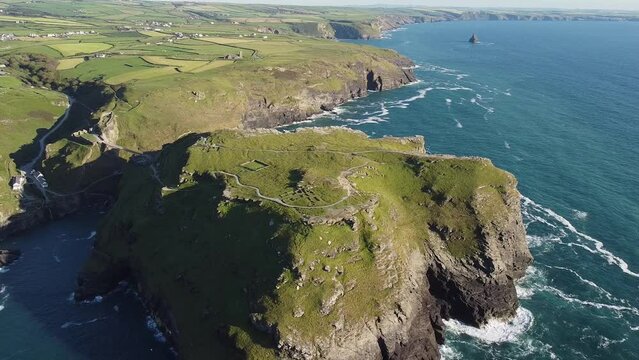 Aerial drone shot of Tintagel, rugged and rocky stretch of coastline with cliffs and rough seas, Cornwall, South West England
