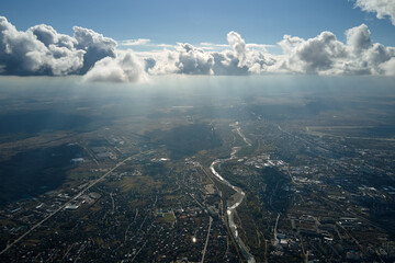Aerial view from airplane window at high altitude of distant city covered with white puffy cumulus...
