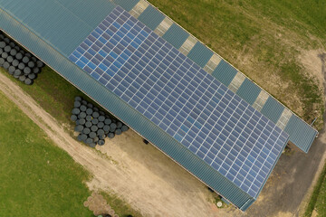 Aerial view of blue photovoltaic solar panels mounted on farm building roof for producing clean...