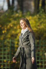 Happy young woman walks in the autumn park. Portrait of a beautiful smiling woman in an elegant gray coat. Pretty woman with light brown hair.