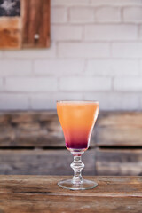 Orange and purple cocktail served on a on a wooden bench patio
