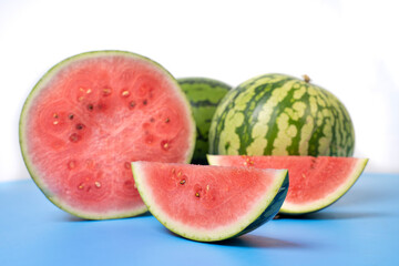 Two whole watermelons and a watermelon cut into smaller pieces. Watermelons with green skin colour and red flesh inside on a white background.