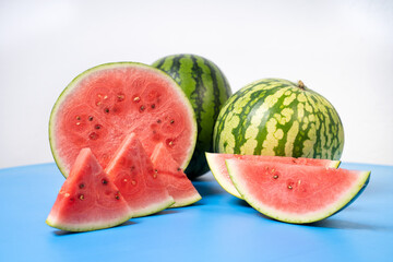 Two whole watermelons and a watermelon cut into smaller pieces. Watermelons with green skin colour and red flesh inside on a white background.