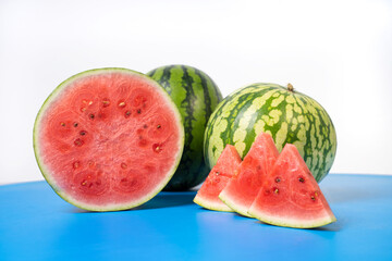 Two whole watermelons and a watermelon cut into smaller pieces. Watermelons with green skin colour and red flesh inside on a white background.