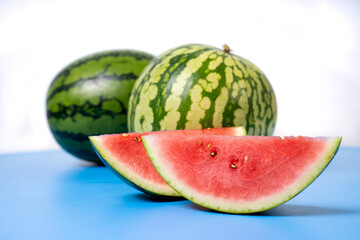 Two whole watermelons and a watermelon cut into smaller pieces. Watermelons with green skin colour and red flesh inside on a white background.