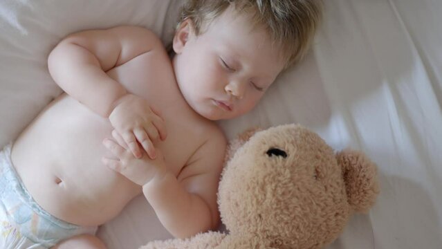 Sleeping baby happy and carefree in bed hugging teddy bear toy. Mother cover with blanket child. Happiness sleep, children without coughing. cute little boy sleeps sweetly in crib sees colorful dream