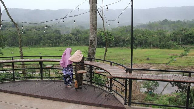 Two women wearing hijab while enjoying the resort atmosphere with views of rice fields and forests