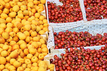 Apricots and cherries in open wooden boxes for sale at the food market.