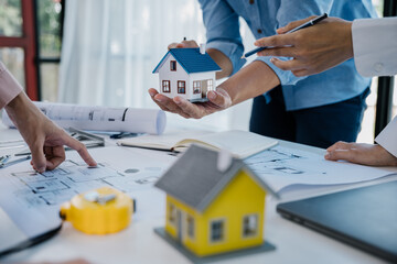 Close up of hands are working on home model mock-up, plan drawings, engineer and architectural tools, paperworks that show architectural, engineering, and work details.