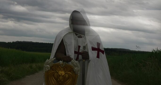 Black male warrior Angel with shifting clouds over face kneeling in the field in Knight's Templar clothing as weather speeds behind, timelapse, Stuttgart Germany, Balvaria Baden Wurttemberg Europe