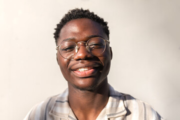 Headshot of young happy and smiling black man wearing glasses outdoors.