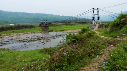 isolated iron suspension bridge over flowing river with mountain and blue sky background at morning
