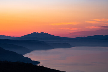 湖を見下ろす夜明けの空と遠くの山のシルエット。日本の北海道の美幌峠の風景。