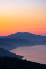 湖を見下ろす夜明けの空と遠くの山のシルエット。日本の北海道の美幌峠の風景。