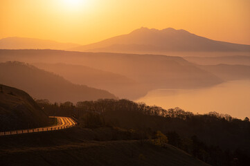 湖と山を背景にした朝陽に照らされた峠道。日本の北海道の美幌峠の風景。