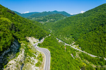 Winding road is meandering between blue sea and green mountains. Aerial view of car driving along the winding mountain road in Sochi, Russia.