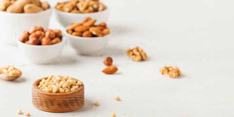 A handful of pine nuts in a bowl on the background of a nut set on a light background. Banner.