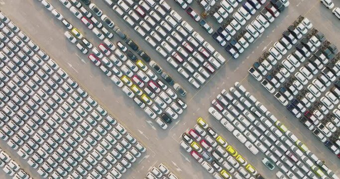 Aerial view of large parking new cars distribution center of modern seaport. Lot of vehicles waiting for sale and transportation shipping by freight cargo vessel ship. Automobile industry.