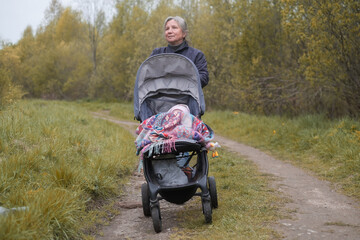 Grandmother walking in spring city park with grandchild with newborn baby in pram.