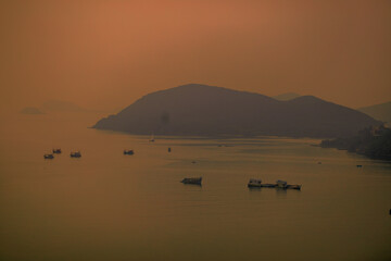 Blurred nature background of the morning sun by the sea, a beautiful golden light, among the trees, rocks and local fishing boats, the beauty of nature during the day.