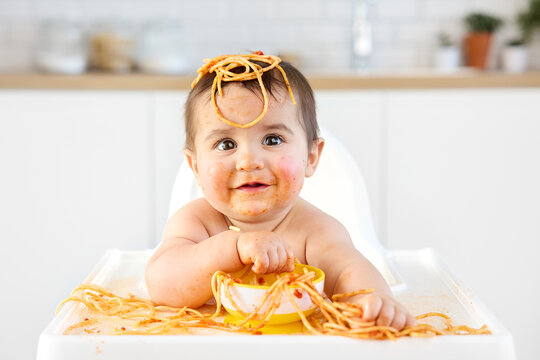 Smiling baby eating spaghetti with his hands