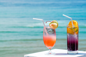 Two cocktails in luxurious hotel at sunny summer day. Mocktail drinks with straws in luxury tropical resort. Travel, vacations, holidays or tourism concept. Turquoise sea waves background. Copy space.