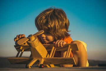 Child pilot with toy airplane dreams of traveling in summer in nature. Kids dreams. Child plays with a toy plane and dreams of becoming a pilot. Cute kids face.