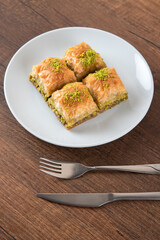 Pistachio baklava in a white plate on wooden background

