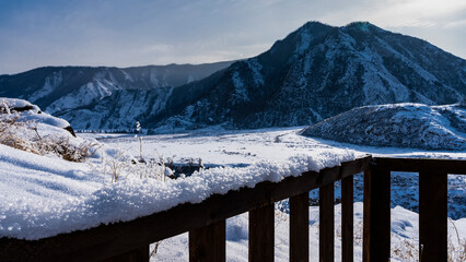 There is a layer of snow and fluffy frost on the railing of the wooden fence. In the distance,...