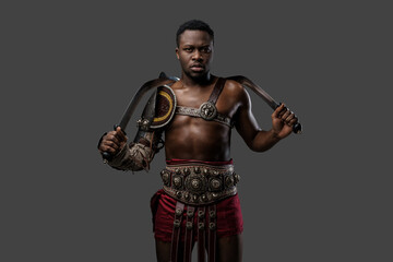 Fototapeta na wymiar Shot of antique gladiator of african descent holding dual swords isolated on gray background.