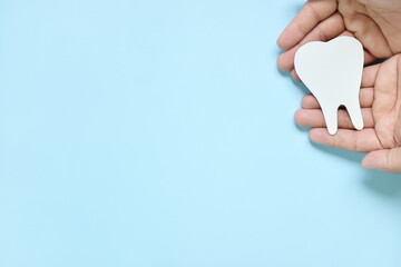 Top view of hands holding a big white tooth cutout in blue background with copy space. Oral and dental care concept.