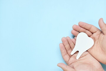 Top view of hands holding a big white tooth cutout in blue background with copy space. Oral and...
