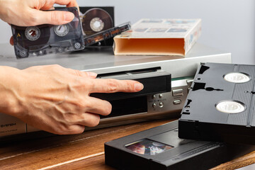 hand holds magnetic audio tape cassette for music inserts VHS videocassette into video recorder