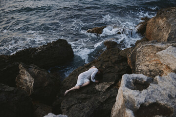 beautiful young woman in a secluded spot on a wild rocky coast in a white dress unaltered