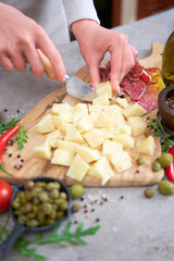 Woman chopping Parmesan cheese with knife on grey table at domestic kitchen