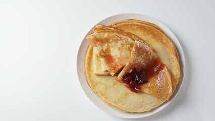 French crepes for Breakfast with strawberry jam.  Wheat golden yeast pancakes or crepes in a white plate closeup.